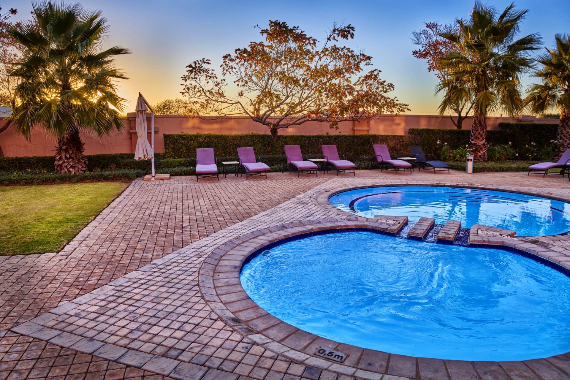 Curved hotel pool with loungers and palm trees at sunset at Rio, Klerksdorp